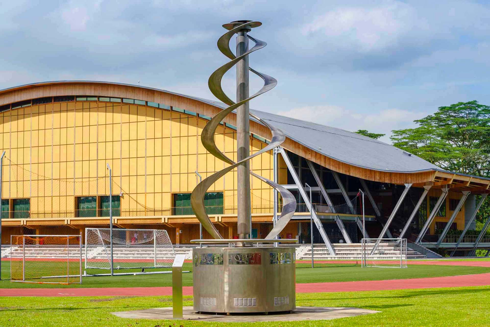 Spiral stainless steel sculpture on grass in front of yellow SRC building