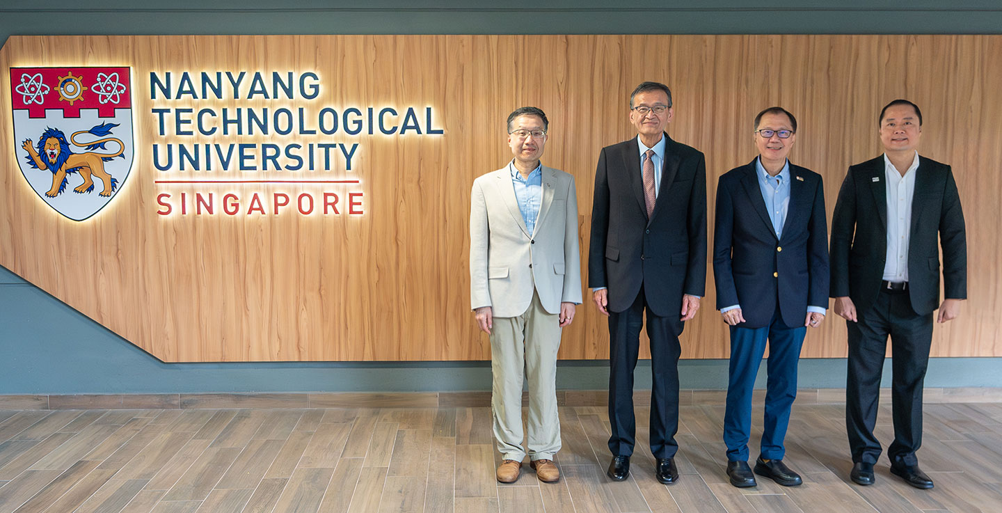 Photo of professors and alumni standing infront of a wall with NTU logo.