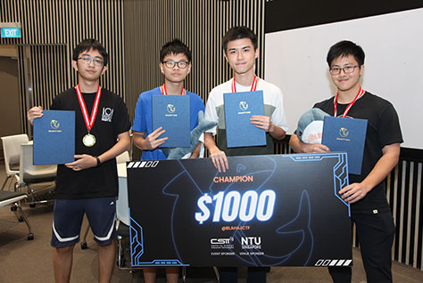 Photo of a winning team of four JC students holding a big prize cardboard.