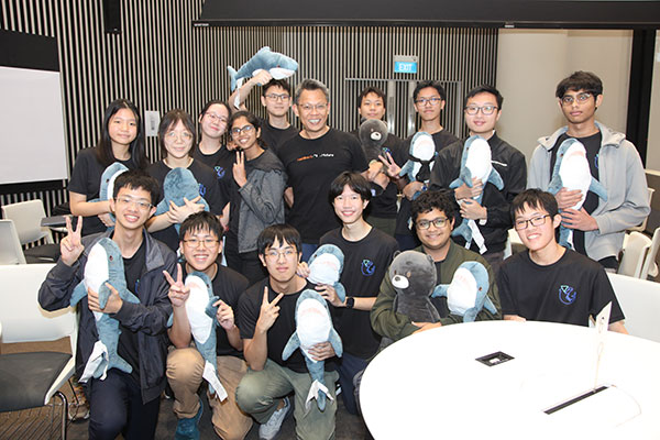 Photo of a group of JC students, each holding a stuffed toy shark infront of a camera.