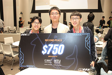 Photo of a group of three JC students, 2nd prize winners, holding a big prize cardboard.