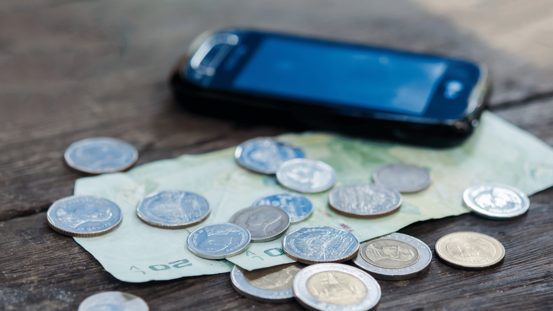 Mobile phone in the background with coins and dollar note beside it