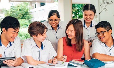 Smiling Female Teacher in Orange Dress with Group of 5 Secondary Students in Uniform Studying with Textbooks