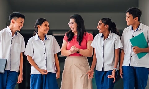 Walking Chinese Lady Teacher Red Top and Ivory Skirt Walking Along School Campus With Group Of 4 Secondary Students In School Uniform Closeup (720x432px)