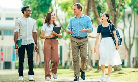 Walking Male Caucasian Teacher Blue Shirt in Main NTU Campus Grounds with 3 Young Adult Students Girl with Brown Pants (720x432px)